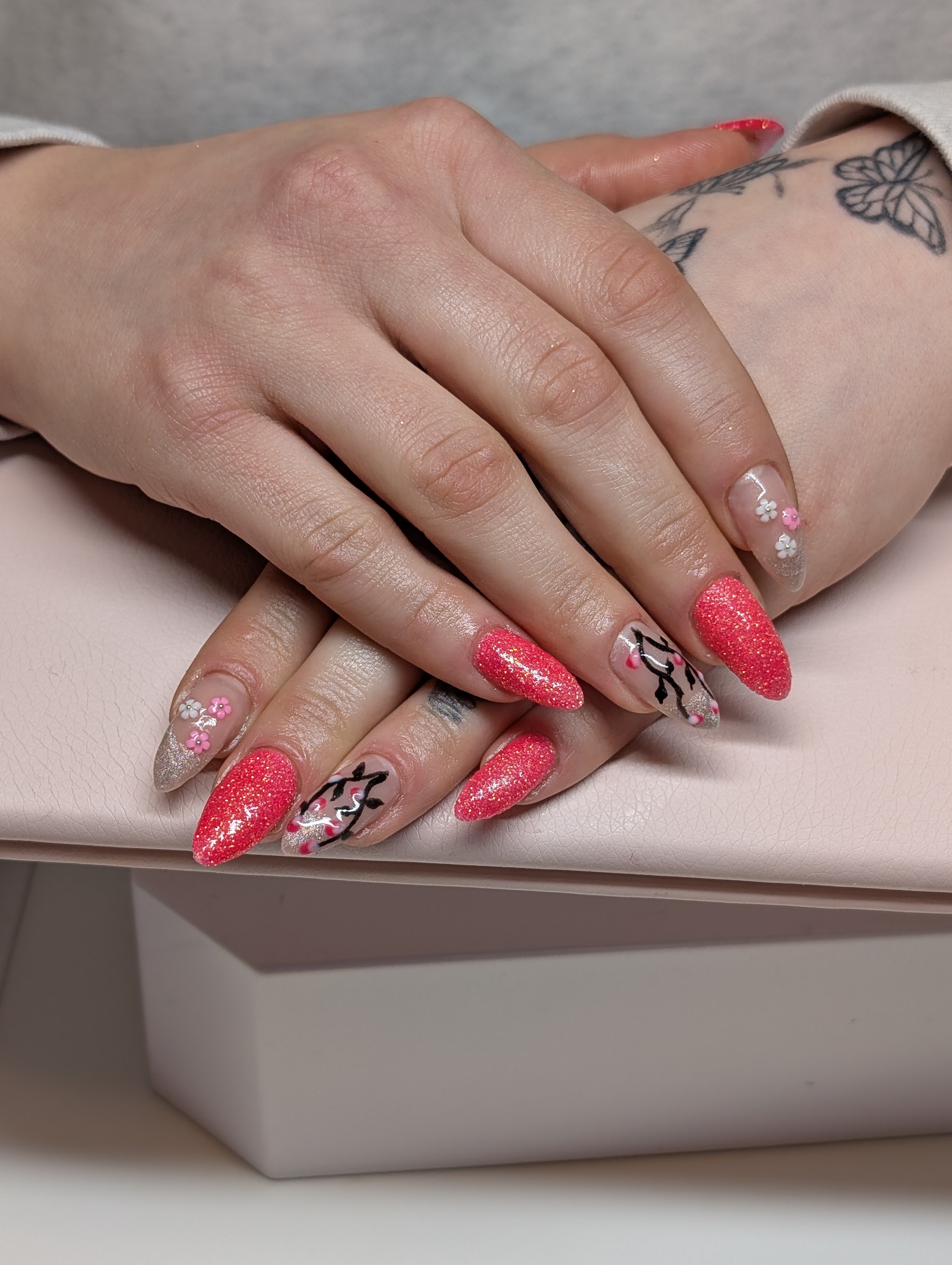 Koraalroze glitternagels met bloemen en een zwart motief